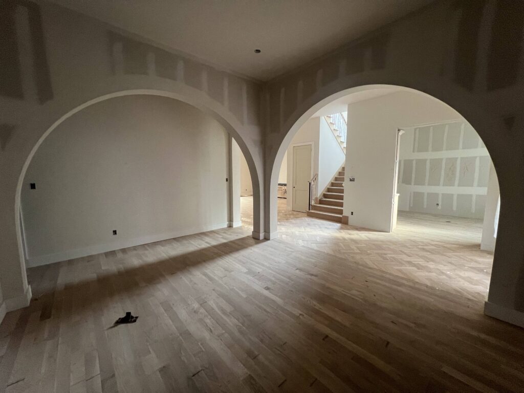 Arched doorways leading toward a staircase in an unfinished new construction home, before paint and flooring