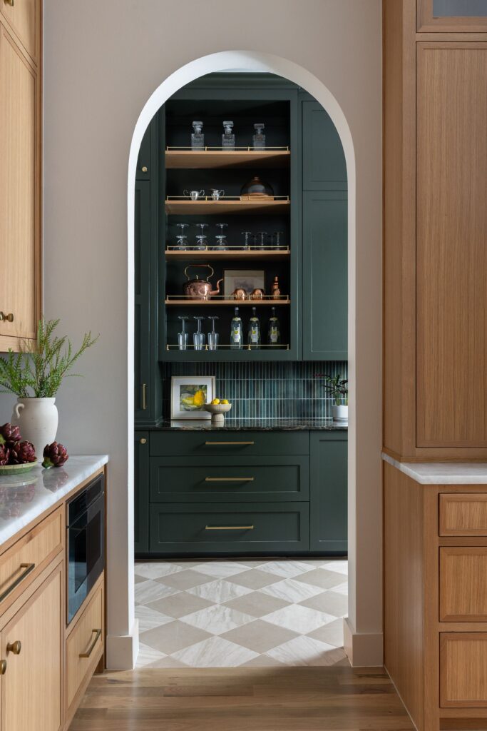 Arched butler's pantry with deep green cabinetry, brass hardware, and glassware styled on open shelving