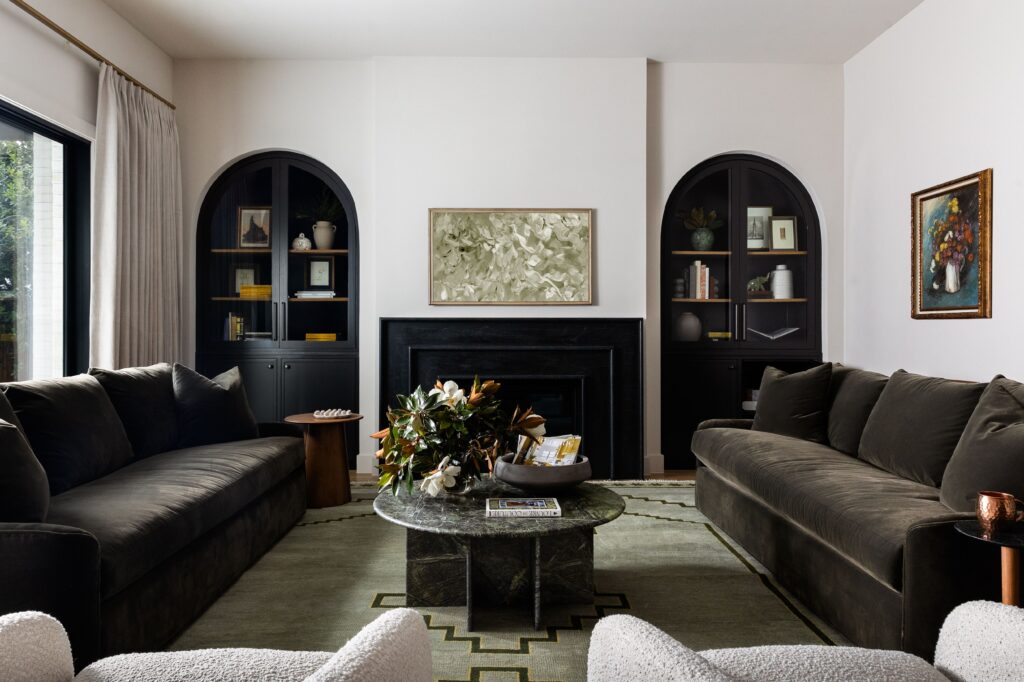 Layered living room with deep green sofas, a marble coffee table, and built-in cabinetry framing a black stone fireplace