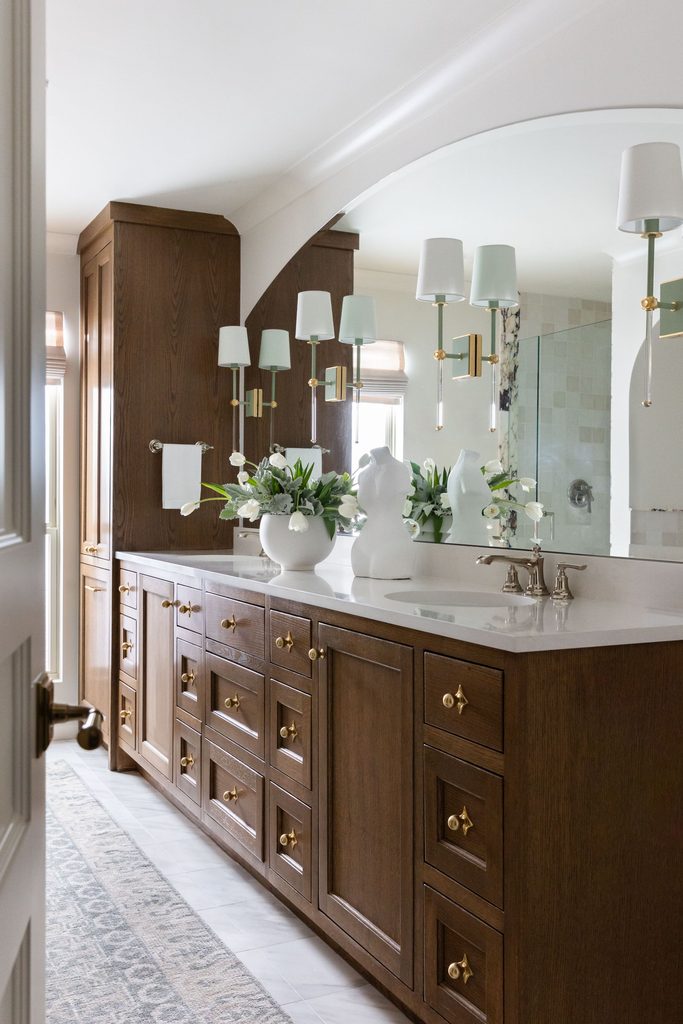Bathroom vanity with wood cabinetry and wall sconces mounted on a large mirror for task lighting, in a Dallas home by Elizabeth Ryan Interiors